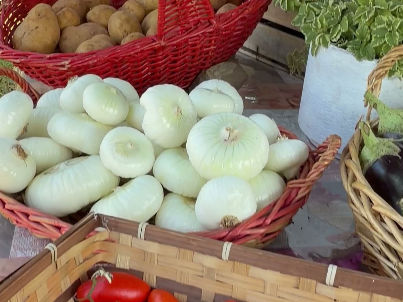 Cipolle bianche mondate in una cesta di vimini accanto a un cesto rosso pieno di patate, sul banco